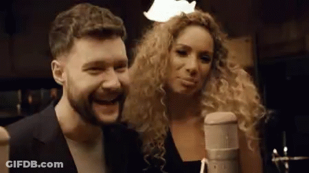 A Man And A Woman Are Singing Into A Microphone . GIF