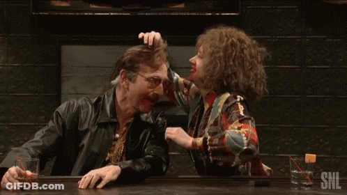 A Man And A Woman Are Sitting At A Bar And The Woman Is Touching The Man 'S Head . GIF