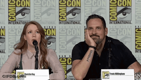 A Man And A Woman Are Sitting At A Comic Con Panel GIF