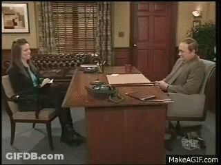 A Man And A Woman Are Sitting At A Desk And Talking To Each Other . GIF