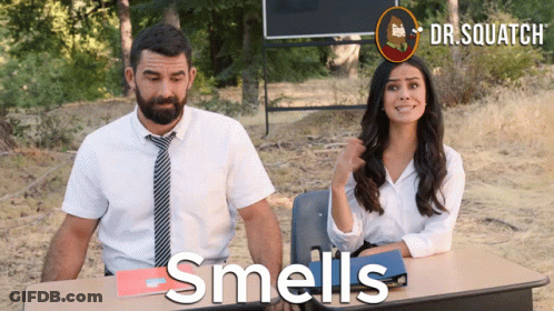 A Man And A Woman Are Sitting At A Desk With The Words Smells Written On The Table GIF