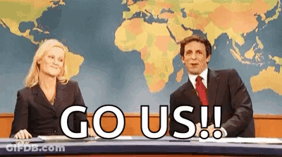 A Man And A Woman Are Sitting At A News Desk With The Words `` Go Us '' Written In Front Of Them . GIF