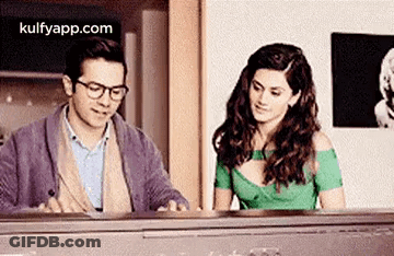 A Man And A Woman Are Sitting At A Piano And Looking At Each Other . GIF