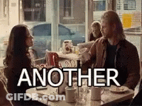 A Man And A Woman Are Sitting At A Table In A Diner With The Word Another Above Them . GIF