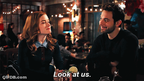 A Man And A Woman Are Sitting At A Table In A Restaurant And The Man Is Saying Look At Us GIF