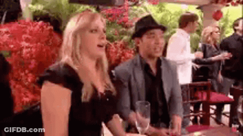 A Man And A Woman Are Sitting At A Table In A Restaurant . The Woman Is Wearing A Hat . GIF