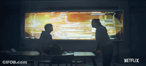 A Man And A Woman Are Sitting At A Table In Front Of A Netflix Sign GIF