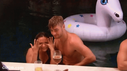 A Man And A Woman Are Sitting At A Table In Front Of An Inflatable Unicorn . GIF