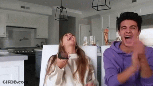 A Man And A Woman Are Sitting At A Table Laughing And Clapping In A Kitchen . GIF