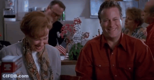A Man And A Woman Are Sitting At A Table Laughing And Smiling . GIF