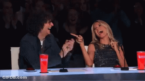 A Man And A Woman Are Sitting At A Table Laughing . The Woman Is Pointing At The Man . GIF