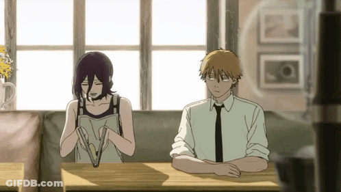A Man And A Woman Are Sitting At A Table Looking At Something . GIF