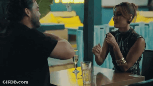 A Man And A Woman Are Sitting At A Table Talking To Each Other . GIF