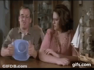 A Man And A Woman Are Sitting At A Table With A Blue Cup . GIF