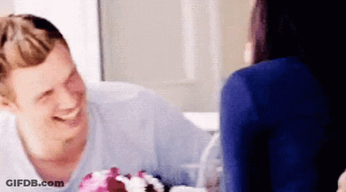 A Man And A Woman Are Sitting At A Table With A Cake On It . GIF