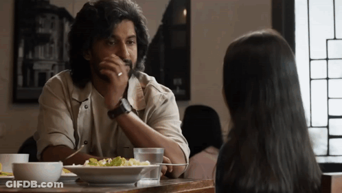 A Man And A Woman Are Sitting At A Table With A Plate Of Food GIF
