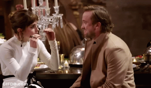 A Man And A Woman Are Sitting At A Table With Candles On It GIF