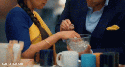A Man And A Woman Are Sitting At A Table With Cups On It GIF