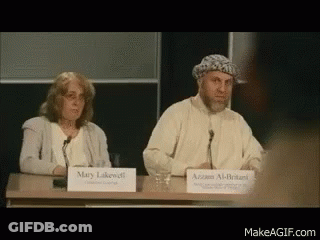 A Man And A Woman Are Sitting At A Table With Signs That Say Mary Lakewell And Azzam Al-Britanni GIF