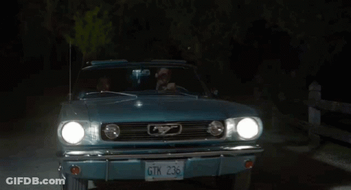 A Man And A Woman Are Sitting In A Blue Car At Night GIF
