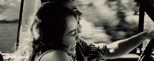A Man And A Woman Are Sitting In A Car And Laughing . GIF
