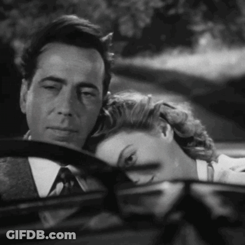 A Man And A Woman Are Sitting In A Car And The Woman Is Resting Her Head On The Man 'S Steering Wheel GIF