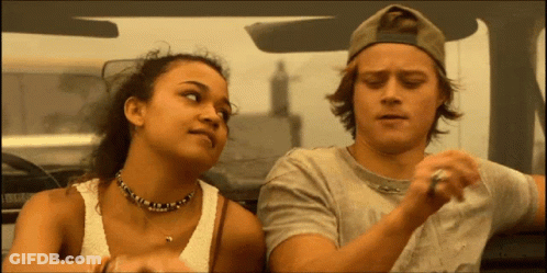 A Man And A Woman Are Sitting In A Car And The Woman Is Wearing A Necklace GIF