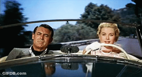 A Man And A Woman Are Sitting In A Car Looking At Each Other GIF