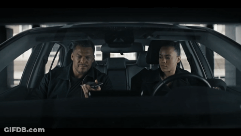 A Man And A Woman Are Sitting In A Car Looking At Something GIF