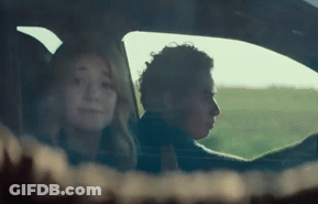 A Man And A Woman Are Sitting In A Car With A Field In The Background . GIF