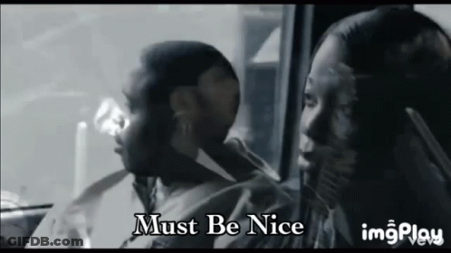 A Man And A Woman Are Sitting In A Car With The Words Must Be Nice On The Bottom GIF