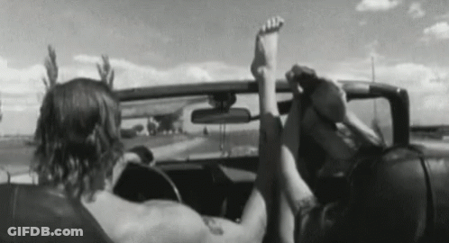 A Man And A Woman Are Sitting In A Car With Their Feet Up In The Air . GIF