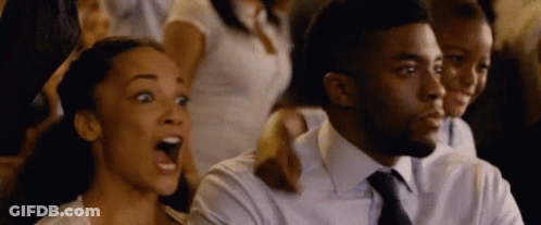 A Man And A Woman Are Sitting In A Crowd With Their Mouths Wide Open GIF