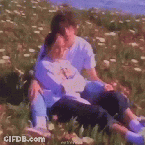 A Man And A Woman Are Sitting In A Field Of Flowers And Hugging Each Other . GIF
