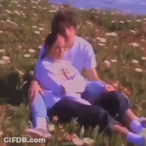 A Man And A Woman Are Sitting In A Field Of Flowers And Hugging Each Other . GIF