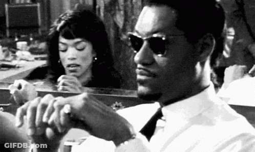 A Man And A Woman Are Sitting In Front Of A Mirror . The Man Is Wearing Sunglasses . GIF
