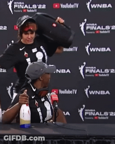 A Man And A Woman Are Sitting In Front Of A Wall That Says Wnba Finals 22 GIF