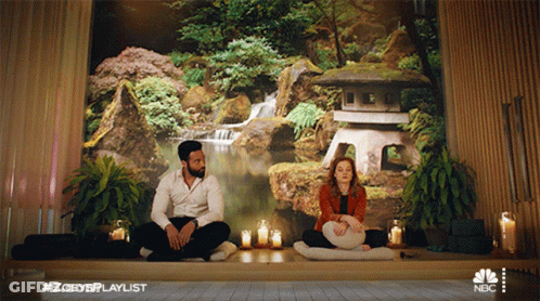 A Man And A Woman Are Sitting In Front Of A Wall With A Waterfall In The Background GIF