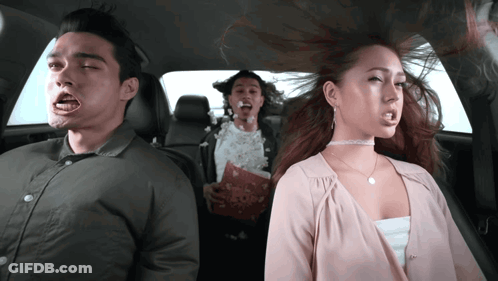 A Man And A Woman Are Sitting In The Back Seat Of A Car With Popcorn In Their Mouths GIF