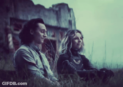 A Man And A Woman Are Sitting In The Grass Looking At Something . GIF