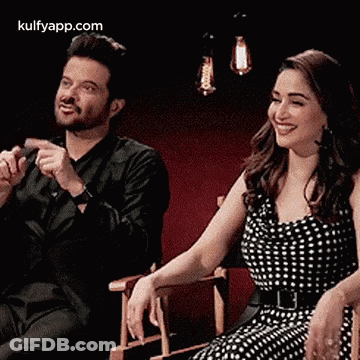 A Man And A Woman Are Sitting Next To Each Other And Smiling . GIF
