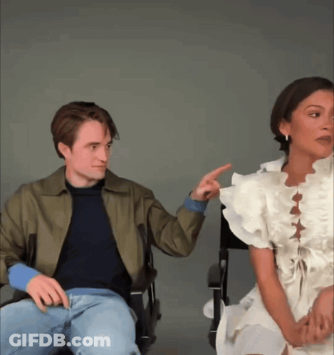A Man And A Woman Are Sitting Next To Each Other And The Woman Is Pointing At The Man GIF