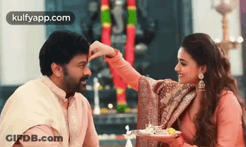 A Man And A Woman Are Sitting Next To Each Other And The Woman Is Putting Something On The Man 'S Face . GIF