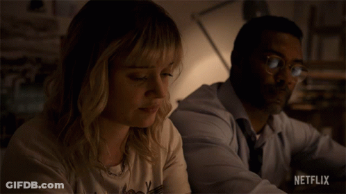 A Man And A Woman Are Sitting Next To Each Other And The Woman Is Wearing A Netflix Shirt GIF