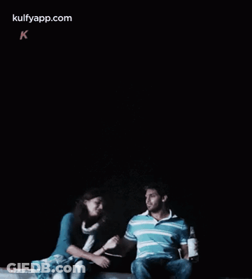 A Man And A Woman Are Sitting Next To Each Other In A Dark Room .. GIF