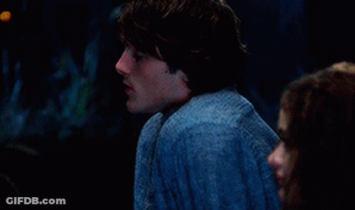 A Man And A Woman Are Sitting Next To Each Other In A Dark Room . The Man Is Wearing A Blue Shirt . GIF