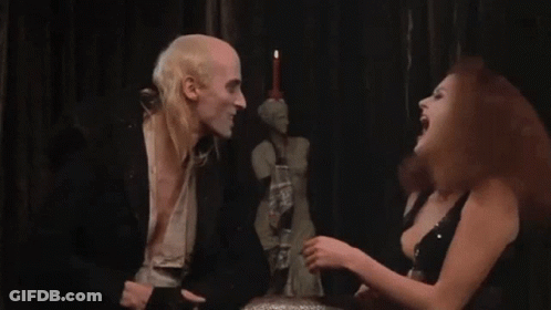 A Man And A Woman Are Sitting Next To Each Other In A Dark Room . The Woman Is Screaming At The Man . GIF