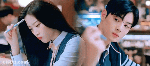 A Man And A Woman Are Sitting Next To Each Other In A Restaurant . The Woman Is Holding A Pen In Her Hand . GIF