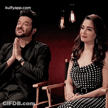 A Man And A Woman Are Sitting Next To Each Other In Chairs . GIF