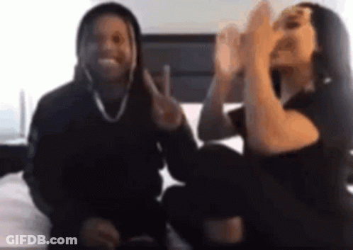 A Man And A Woman Are Sitting Next To Each Other On A Bed And Making Peace Signs . GIF